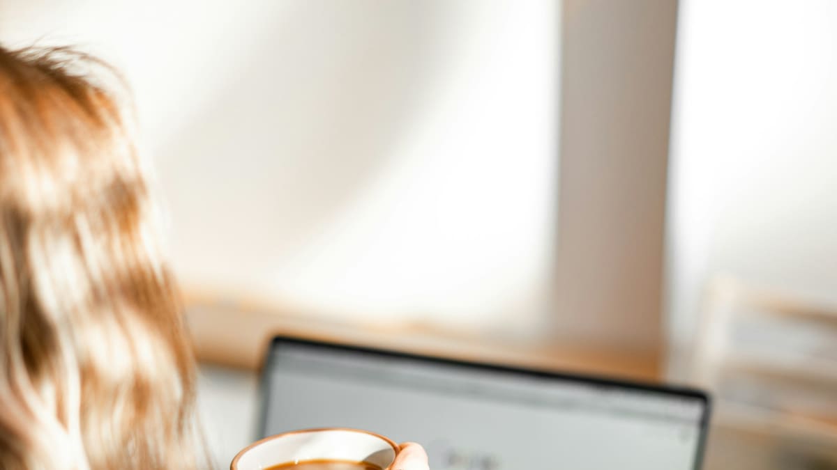 Woman holding a cup in front of a laptop